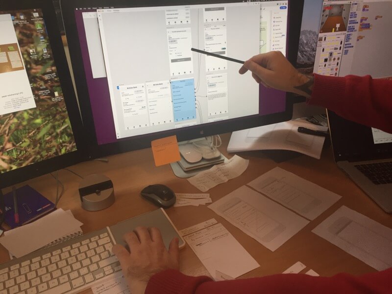 The team working over a monitor displaying the app screens mapped into Adobe XD prototyping software showing connections